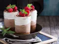 Tre deliziosi bicchierini di dolce freddo al cioccolato e panna, guarniti con lamponi freschi e scaglie di cioccolato.
