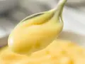 Crema pasticcera lucida su un cucchiaio. Il burro la rende vellutata e lucida, perfetta per farcire dolci.