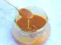Un cucchiaio raccoglie un denso caramello salato da un barattolo di vetro. La salsa dorata cola lentamente, invitando a un assaggio goloso.
