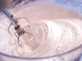 Frusta elettrica che lavora per montare a neve albumi in una ciotola di vetro, creando una soffice meringa.