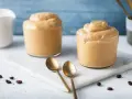Due bicchieri di soffice crema di caffè, perfetta ricetta crema di caffè senza panna e senza caffè solubile. Due cucchiaini dorati e chicchi di caffè completano la scena.