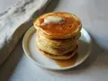 Pancakes dorati e soffici, impilati su un piatto bianco, con una noce di burro che si scioglie in cima e sciroppo d'acero che cola. Sembrano pronti per essere gustati, un vero piacere per gli occhi e per il palato, come un pancake in bottiglia pronto d...
