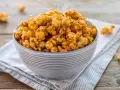 Una ciotola piena di pop corn caramellati, dorati e invitanti, su un tovagliolo a righe.