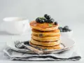 Pancake con farina di riso, guarniti con mirtilli freschi e sciroppo d'acero, su un piatto rustico con forchetta.
