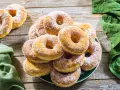 Un piatto pieno di graffe napoletane, dolci soffici e dorati, cosparse di zucchero a velo, su un tavolo di legno rustico.
