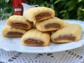 Biscotti nascondini impilati su un piatto bianco, con un ripieno scuro visibile. Sullo sfondo, una moka rossa e foglie verdi.