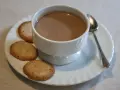 Tazza di crema di cogne fumante con biscotti secchi su un piattino bianco, accompagnata da un cucchiaino.