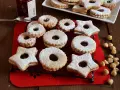 Deliziosi biscotti Linzer, a forma di stella e tondi, ripieni di marmellata e spolverati di zucchero a velo, su una griglia nera.