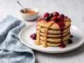 Pila di pancake proteici guarniti con burro d'arachidi, frutti di bosco e marmellata. Una deliziosa ricetta per iniziare la giornata con energia.