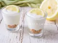 Due bicchierini di mousse al limone con base croccante e fetta di limone, su un tavolo di legno.