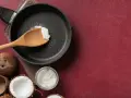Cocco cos'è? Olio di cocco in padella, pronto per cucinare. Freschi cocchi aperti e un vasetto di olio di cocco completano la scena.