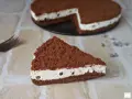 Una fetta di torta al cioccolato con ripieno cremoso al mascarpone e biscotti sbriciolati, decorata con gocce di cioccolato.