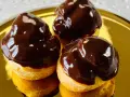 Tre golosi bignè al cioccolato, lucidi e invitanti, su un piatto dorato.