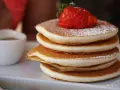 Pancake Bimby perfetti, impilati e spolverati di zucchero a velo, con una fragola fresca in cima.