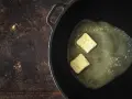 Due cubetti di burro a pomata si sciolgono in una padella, pronti per creare una base saporita.