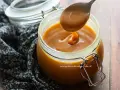 Un cucchiaio raccoglie un denso caramello salato senza panna da un barattolo di vetro.