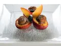 Deliziose pesche ripiene con biscotti e frutti di bosco, un dolce invitante su un piatto di vetro.