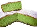 Una fetta di torta alla menta verde brillante, cosparsa di zucchero a velo, è appoggiata su una torta intera.