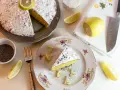 Una fetta di torta al limone cosparsa di zucchero a velo e semi di papavero, guarnita con spicchi di limone fresco.