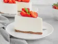 Una fetta di torta fredda allo yogurt senza biscotti, guarnita con fragole fresche e menta, su un piatto bianco.