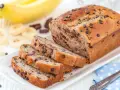 Fette di plumcake banana e cioccolato su un piatto bianco, con banane e gocce di cioccolato sullo sfondo.
