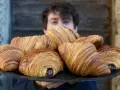 Un ragazzo sorride dietro un vassoio pieno di croissant brioche dorati e fragranti, alcuni con ripieno di cioccolato.