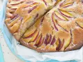 Una deliziosa torta di pesche e yogurt greco, con fette di pesca disposte a raggiera sulla superficie dorata e cosparsa di zucchero a velo.