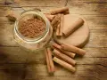 Barattolo di cannella in polvere e bastoncini su un tagliere di legno. Ingredienti essenziali per la cucina.