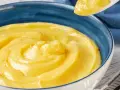 Una ciotola blu piena di deliziosa crema pasticcera senza uova, con un cucchiaio che ne preleva una porzione.