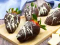Fragole ricoperte di cioccolato fondente e decorate con cioccolato bianco. Un delizioso assaggio di frutta al cioccolato su un tagliere di legno.
