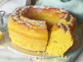 Torta soffice e dorata, spolverata di zucchero a velo, preparata con dolci con eritritolo. Accanto, limoni freschi e un setaccio.