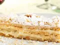 Una fetta di rettangolare torta millefoglie compleanno, con crema pasticcera e zucchero a velo.