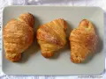 Tre deliziosi croissant dorati, cosparsi di zucchero, disposti su un piatto grigio.