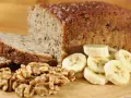 Fetta di banana bread senza uova, con noci e banane a fette, su tagliere di legno.