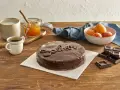 Torta Sacher, un classico viennese, con la sua glassa lucida e il nome scritto in cioccolato. Accanto, albicocche, marmellata e caffè, ingredienti che evocano le sue origini.
