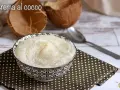 Una ciotola di deliziosa crema al cocco, cosparsa di cocco grattugiato, accanto a gusci di cocco e un cucchiaio.