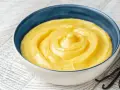 Una ciotola di crema gialla, liscia e invitante, con baccelli di vaniglia accanto. Perfetta per ogni ricetta crema.