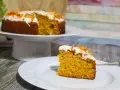Una fetta di torta di carote senza glutine, soffice e profumata, con glassa bianca e decorazioni arancioni.