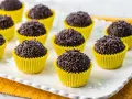 Deliziosi dolcetti brasiliani, brigadeiros al cioccolato, ricoperti di codette, serviti in pirottini gialli su un piatto bianco.