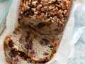 Fetta di banana bread con gocce di cioccolato e noci, guarnita con mandorle e nocciole tritate.