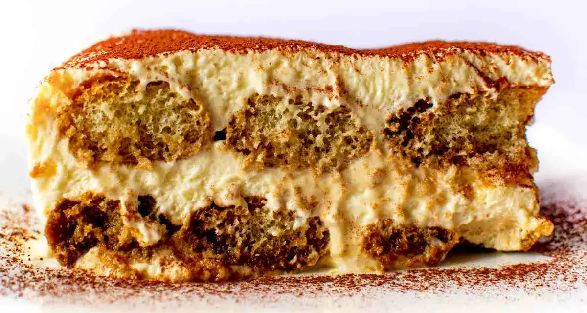 Una fetta di tiramisù, con strati di savoiardi inzuppati e crema al mascarpone, spolverata di cacao. La ricetta perfetta per un dolce indimenticabile.