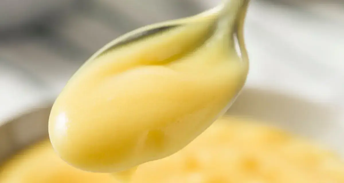 Crema pasticcera lucida su un cucchiaio. Il burro la rende vellutata e lucida, perfetta per farcire dolci.