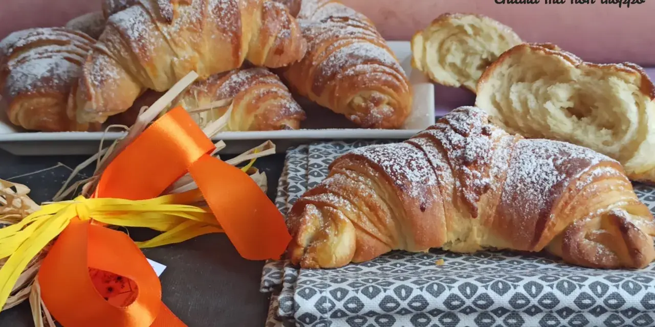 Croissant dorati e soffici, dolci lievitati spolverati di zucchero a velo, pronti per una colazione speciale.