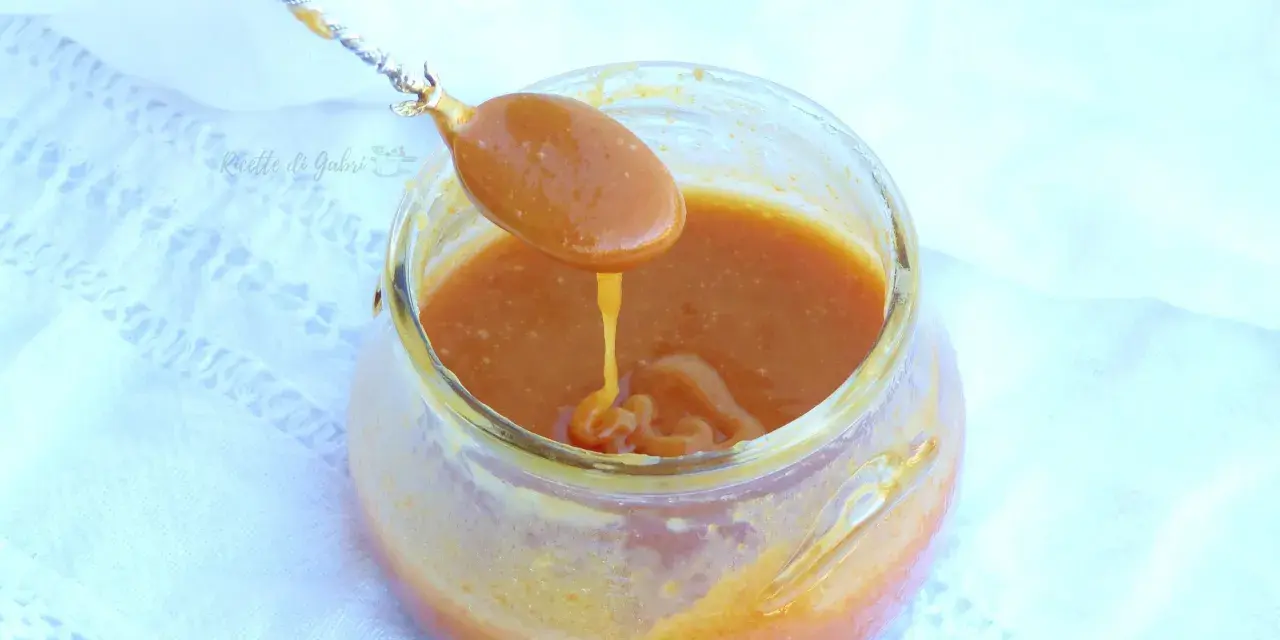 Un cucchiaio raccoglie un denso caramello salato da un barattolo di vetro. La salsa dorata cola lentamente, invitando a un assaggio goloso.