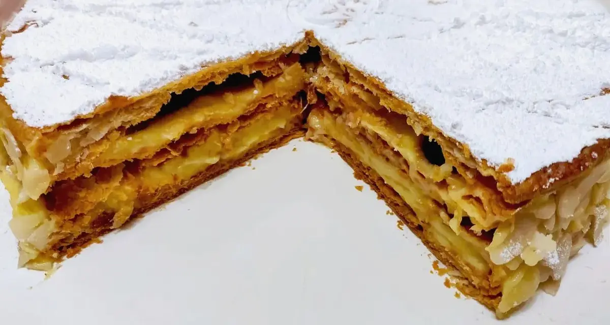 Un delizioso millefoglie alla crema, con strati croccanti di pasta sfoglia e una ricca crema pasticcera, spolverato di zucchero a velo e mandorle.