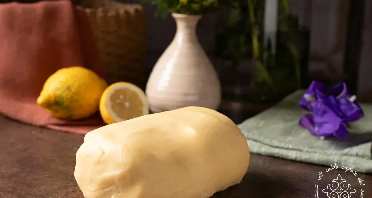 Impasto di pasta frolla che non si rompe, pronto per creare dolci perfetti. Accanto, limoni freschi e un tocco di colore.