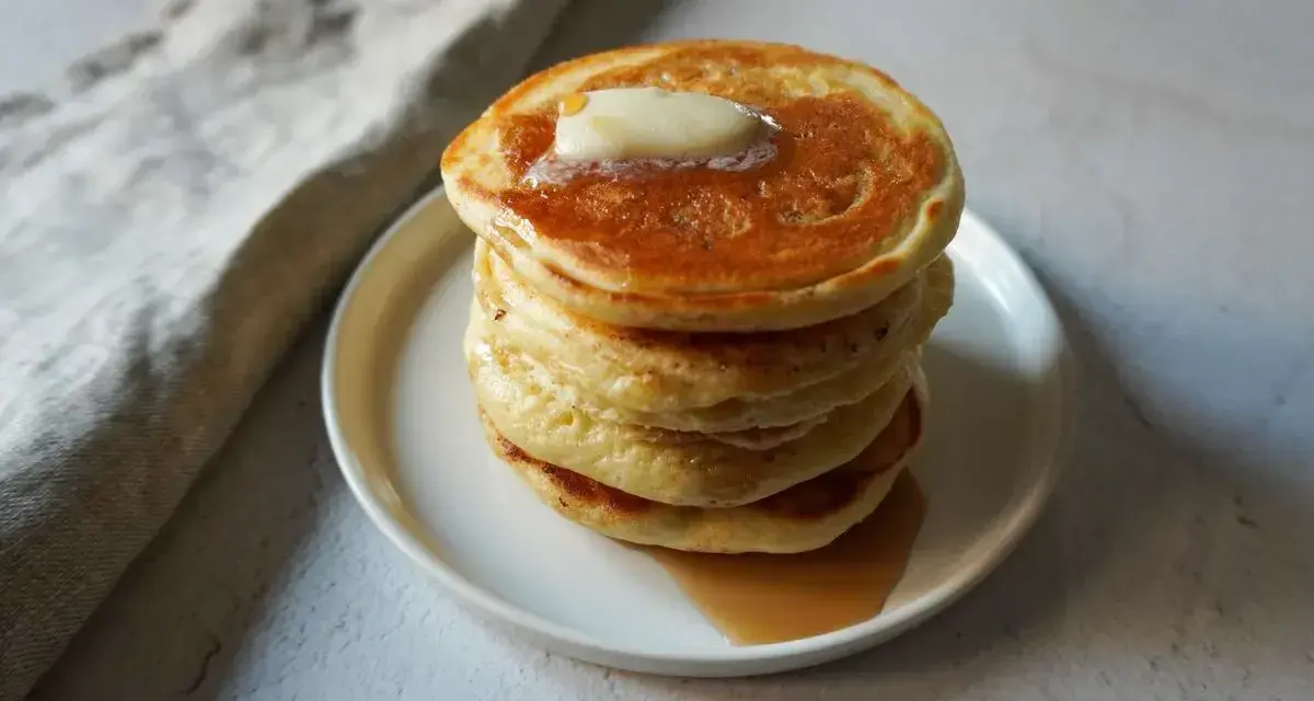 Pancakes dorati e soffici, impilati su un piatto bianco, con una noce di burro che si scioglie in cima e sciroppo d'acero che cola. Sembrano pronti per essere gustati, un vero piacere per gli occhi e per il palato, come un pancake in bottiglia pronto d...