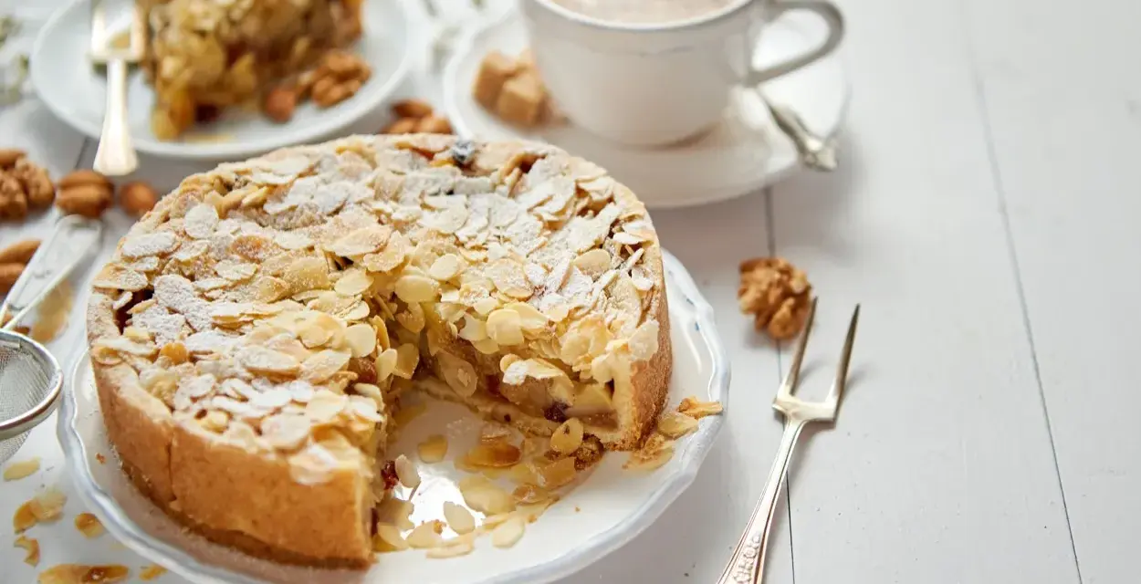 Torta con mandorle e zucchero a velo, perfetta per una ricetta frangipane. Accanto, una tazza di caffè e una fetta di torta.