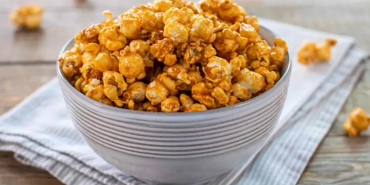 Una ciotola piena di pop corn caramellati, dorati e invitanti, su un tovagliolo a righe.