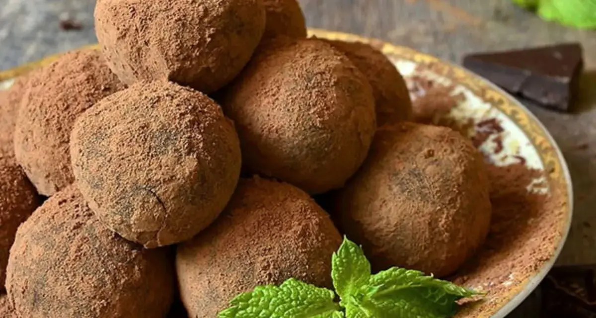 Pile di tartufi al cioccolato facili e veloci, spolverati di cacao, con menta fresca e un pezzetto di cioccolato fondente.